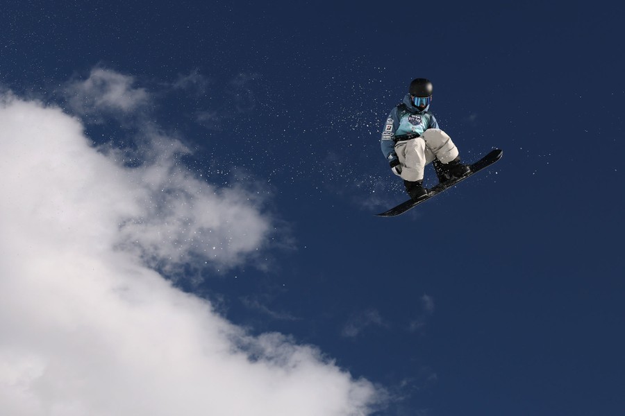 A snowboarder, mid-jump, against a blue sky and clouds