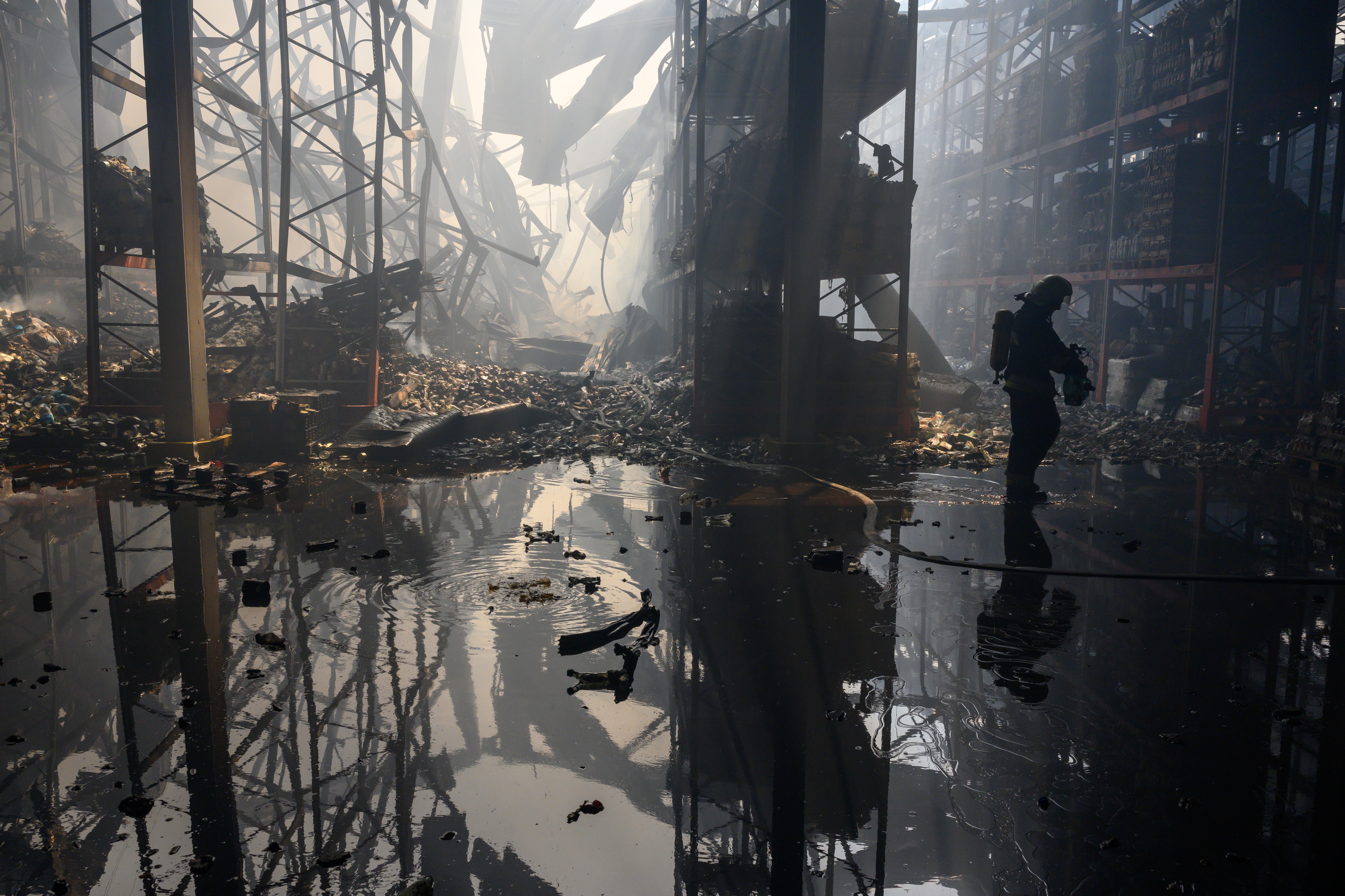 A firefighter walks through the wet and smoky ruins of a warehouse following a bomb attack.
