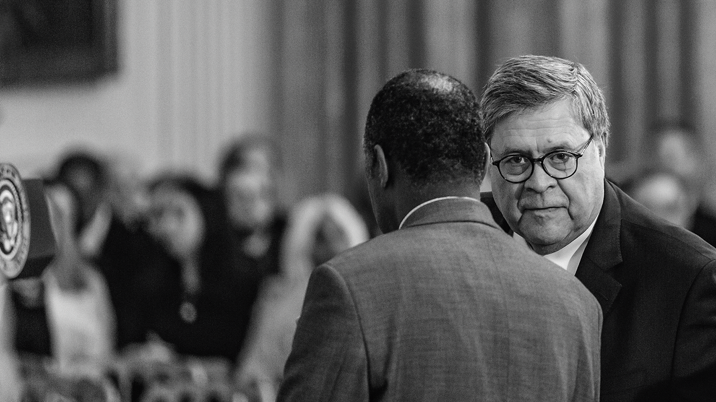black-and-white photo of Bill Barr and Ben Carson conferring with each other with audience in background