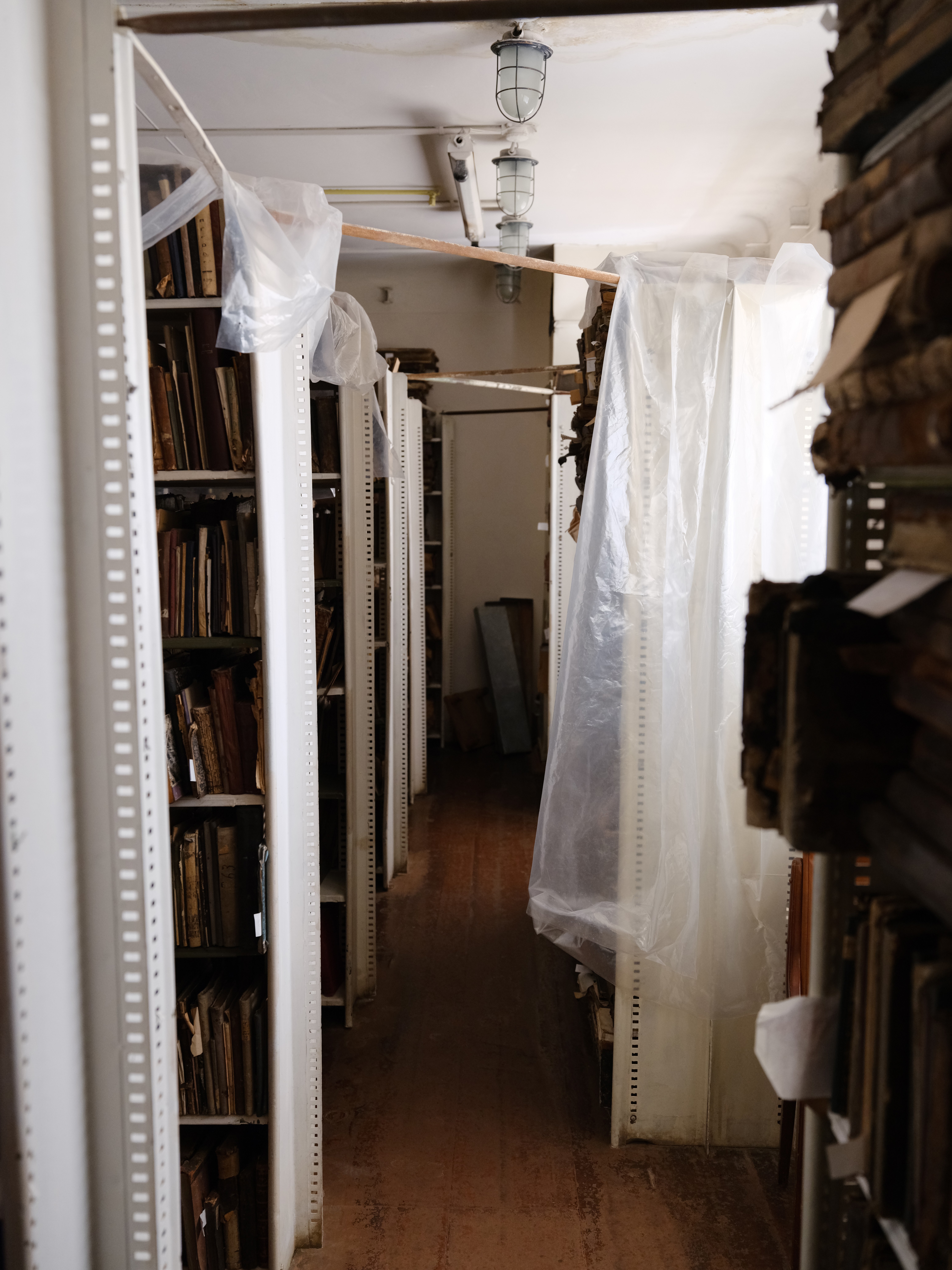 photo of room with wooden floor and shelves of books, with clear plastic sheets hanging over many of them