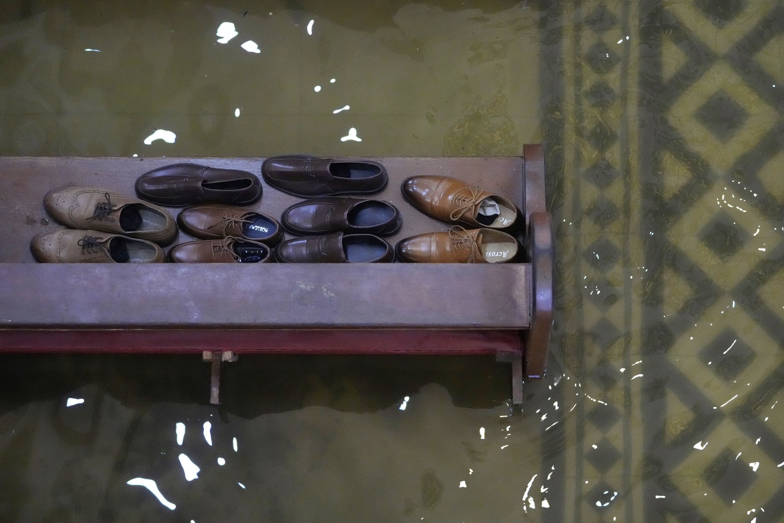 A top-down view of several pairs of shoes on a church pew, surrounded by shallow floodwater