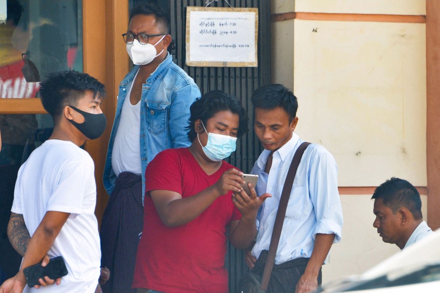 Several people stand together outside a shop, looking at a mobile phone.