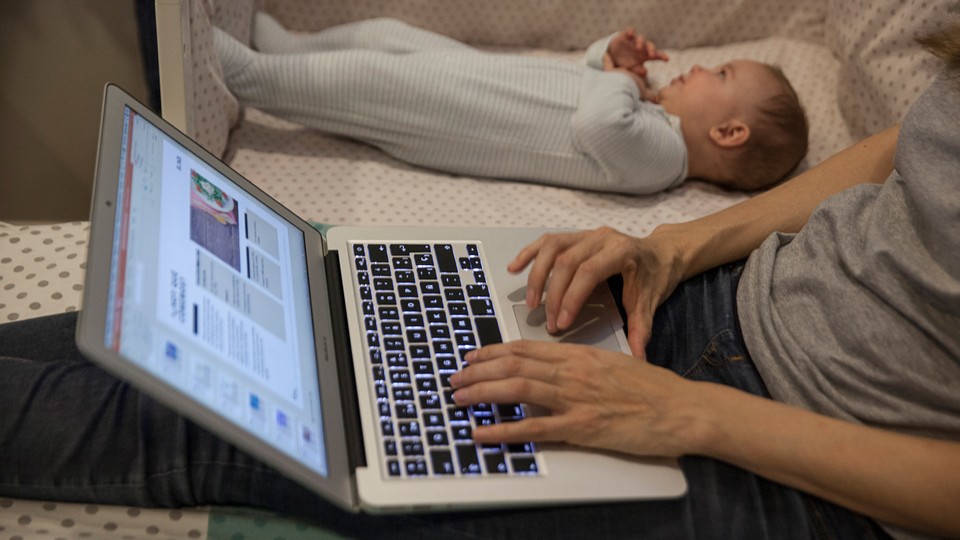 Photo showing a person working on a laptop, sitting on the floor next to a baby