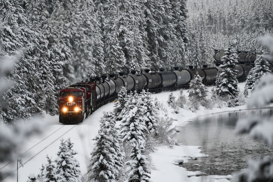 A locomotive pulls a train through a snowy mountain scene.