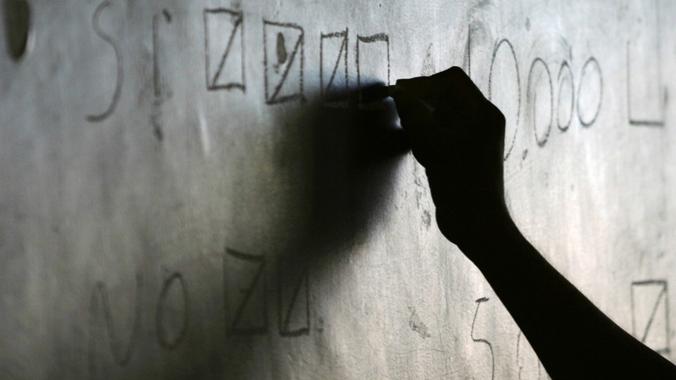 A silhouette hand writes on a chalkboard.
