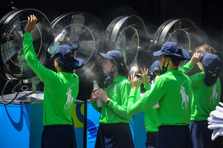 Young people stand in front of water misters and fans, cooling off.