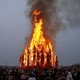 A crowd gathers around a burning temporary wooden structure during a festival.