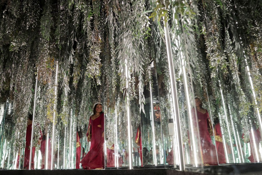 A person walks through an exhibition space filled with large glass tubes and hanging plants.