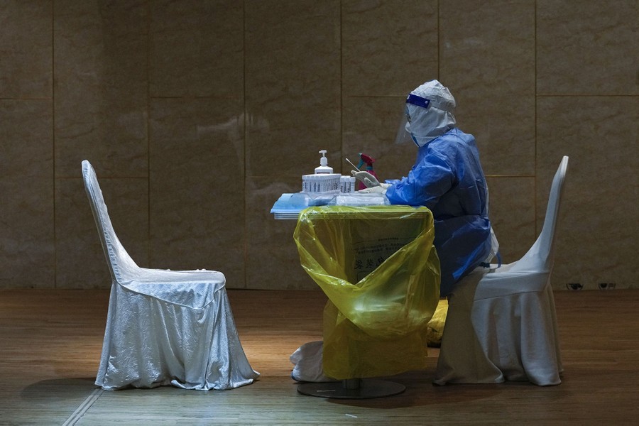 A medical worker in protective gear sits at a small table and waits to administer COVID-19 tests.