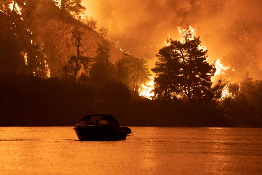 A boat is seen on water at night, with a raging wildfire in the background.