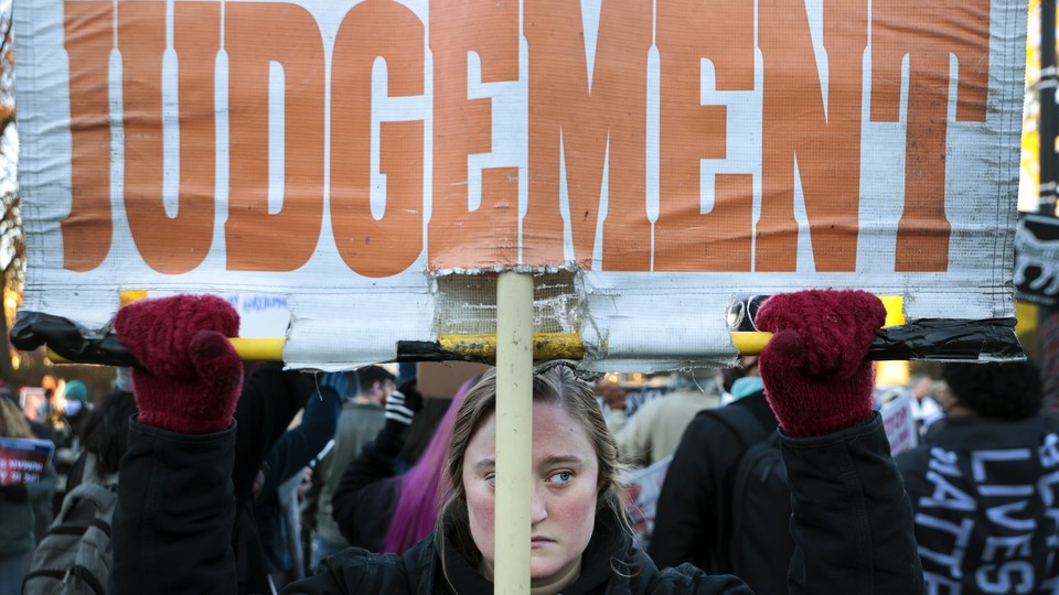 A photo of a protester holding a sign that reads "Judgement" in orange letters on a white background