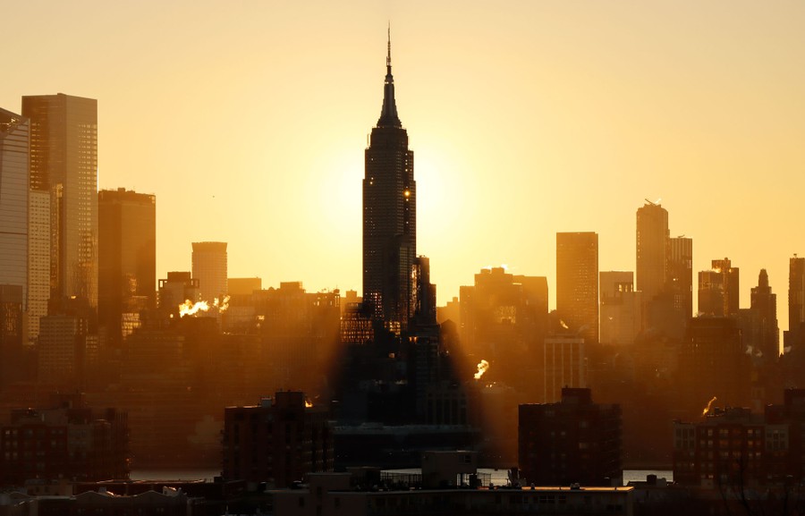 The Empire State Building casts a shadow as the sun rises behind it.