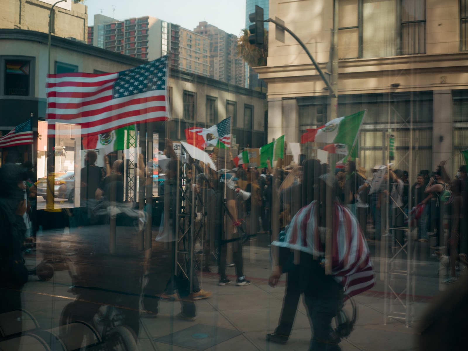 In a reflection through a window people are seen marching with American and Mexican flags in Los Angeles