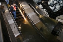 A man in a construction vest stands on a flooded escalator in a subway station.