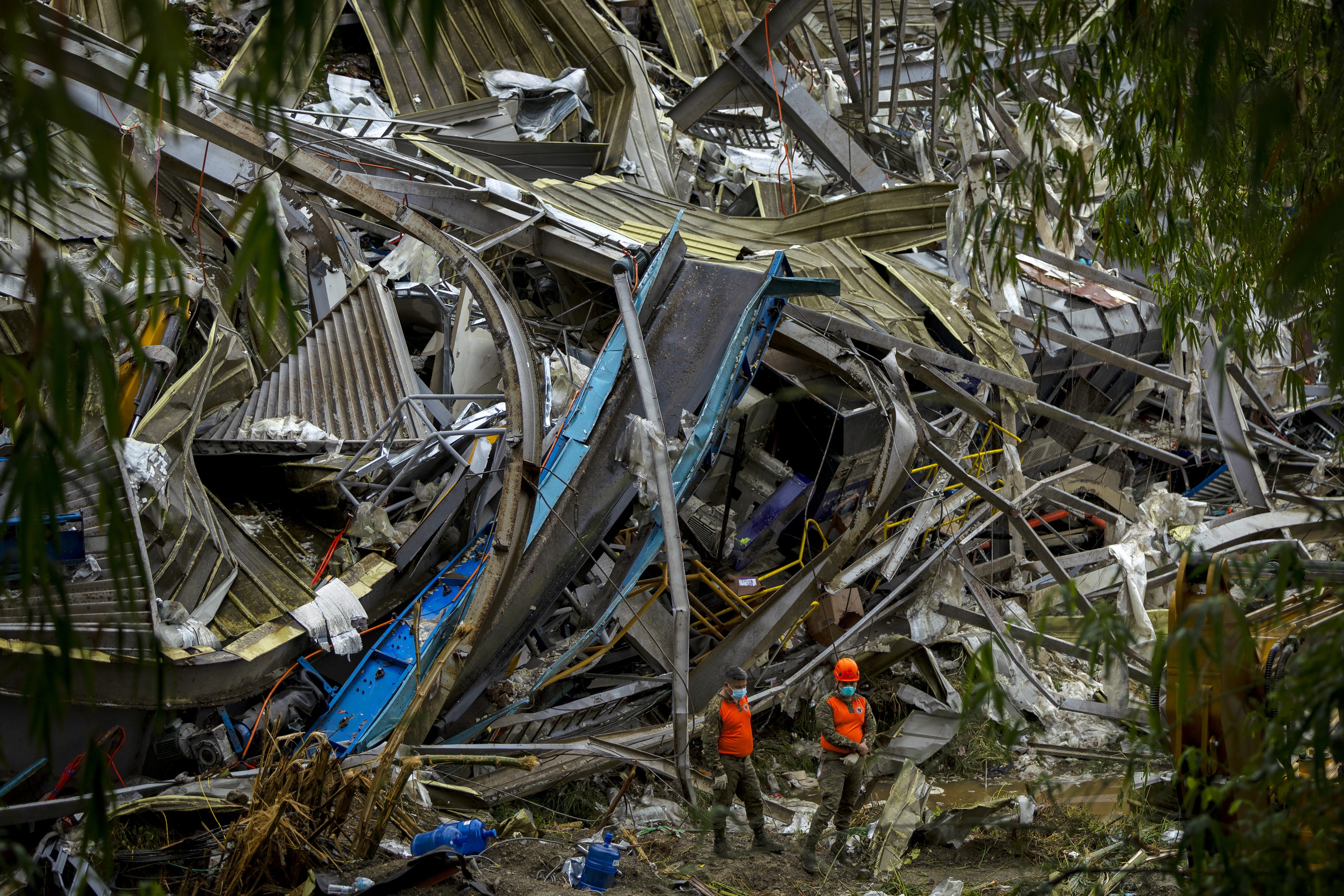 Two rescue workers stand beside a giant pile of debris left by a collapsed building.
