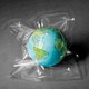 A toy globe inside a plastic shrink wrap bag on a gray floor