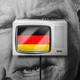 Illustration of an angry man whose face is obscured by a television displaying the German flag