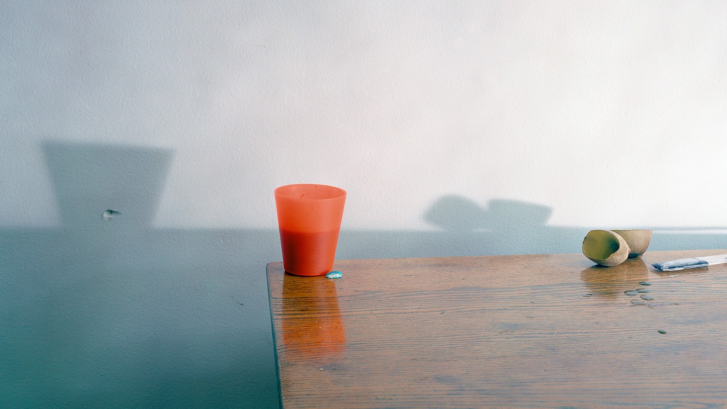 A photo of a red-orange cup on a wooden table, with shadows behind