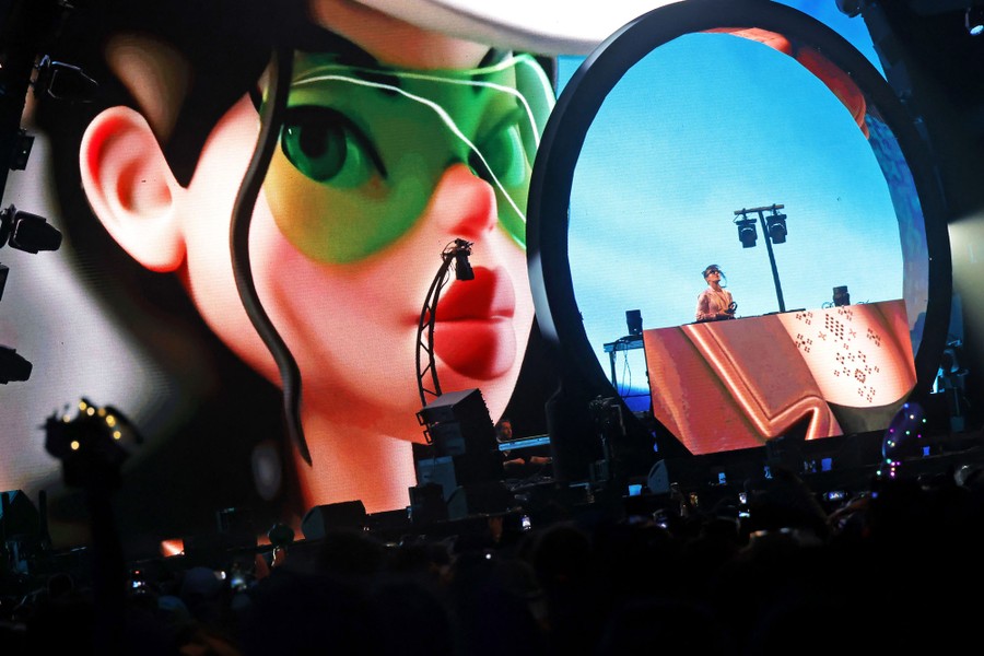A DJ performs, backed by a huge video wall with a cartoonish image of a face.