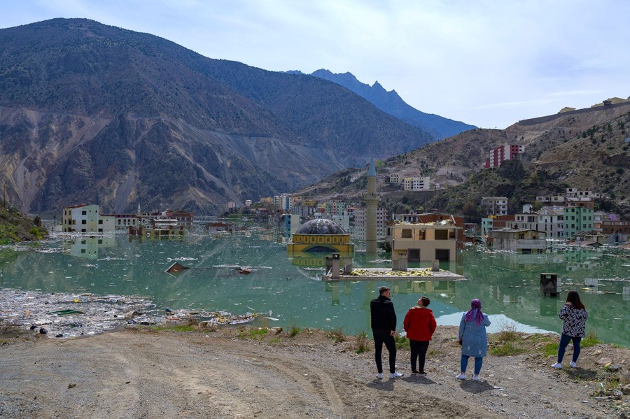 Four people stand on the shore of a reservoir looking out over a town that is being flooded.