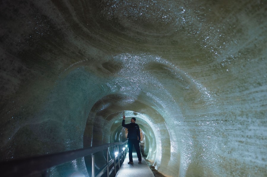 A person walks inside a cave with smooth walls made of ice.