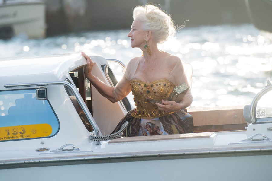 Actor Helen Mirren, dressed up, rides a small boat in Venice.