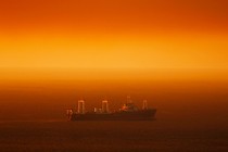 A large ship travels across a stretch of ocean that appears red in the sunlight