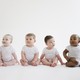 Five racially diverse babies sitting in a line wearing white onesies
