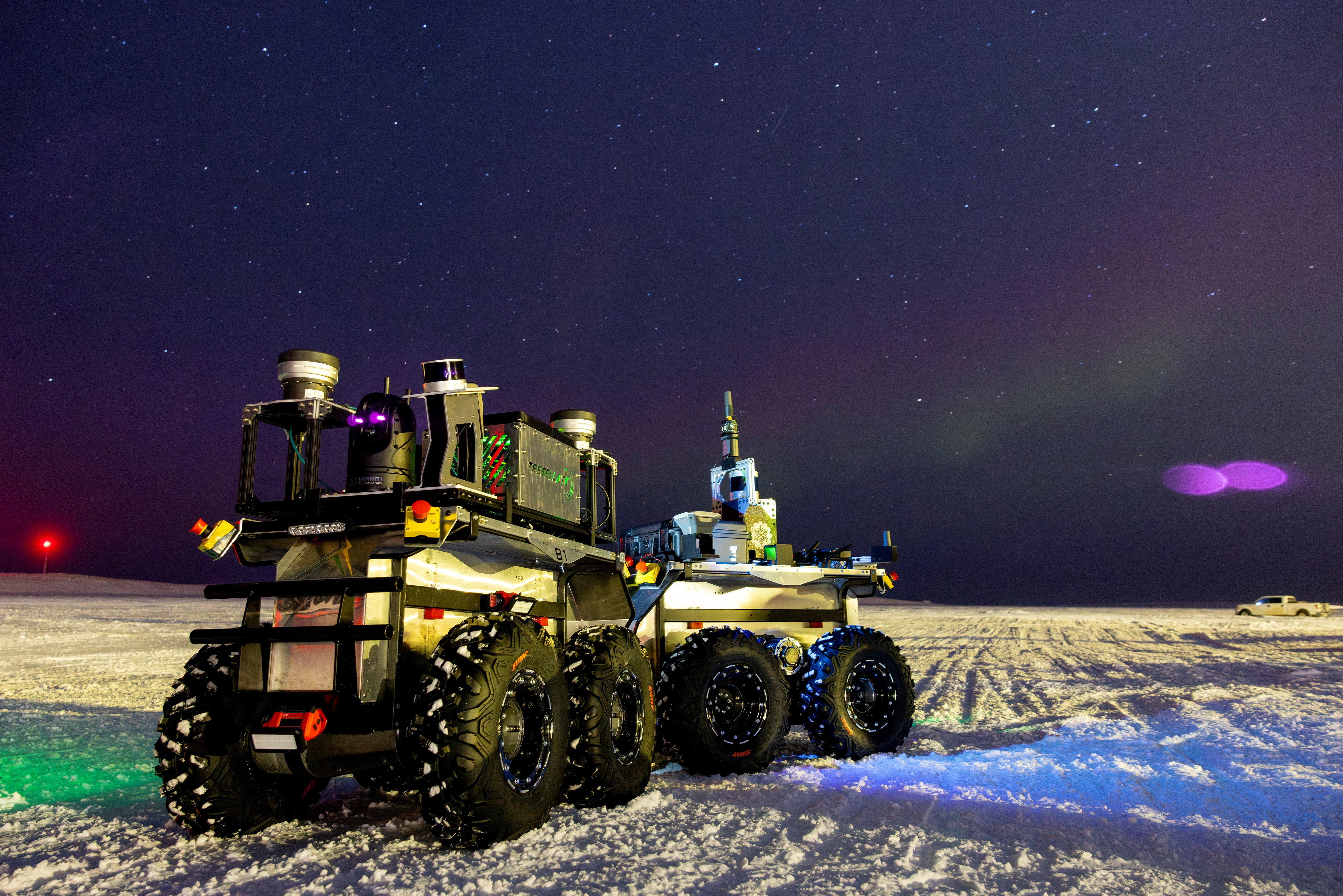 An autonomous eight-wheeled robot sits on a snow-covered plain at night.