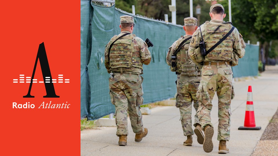 A color photograph of uniformed National Guard troops carrying guns while walking down a sidewalk in Washington, D.C.