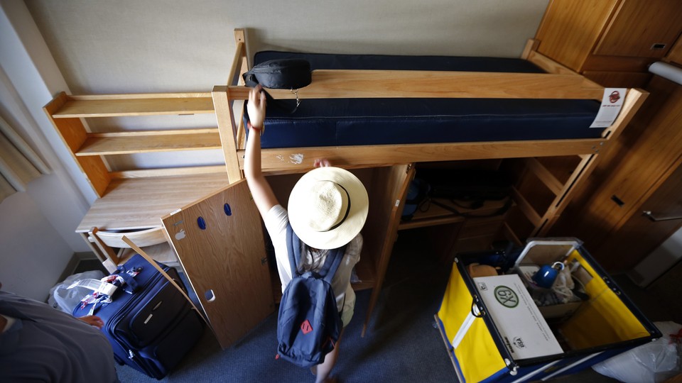 A student sets up her twin-sized bed and arranges other items in her dormitory.