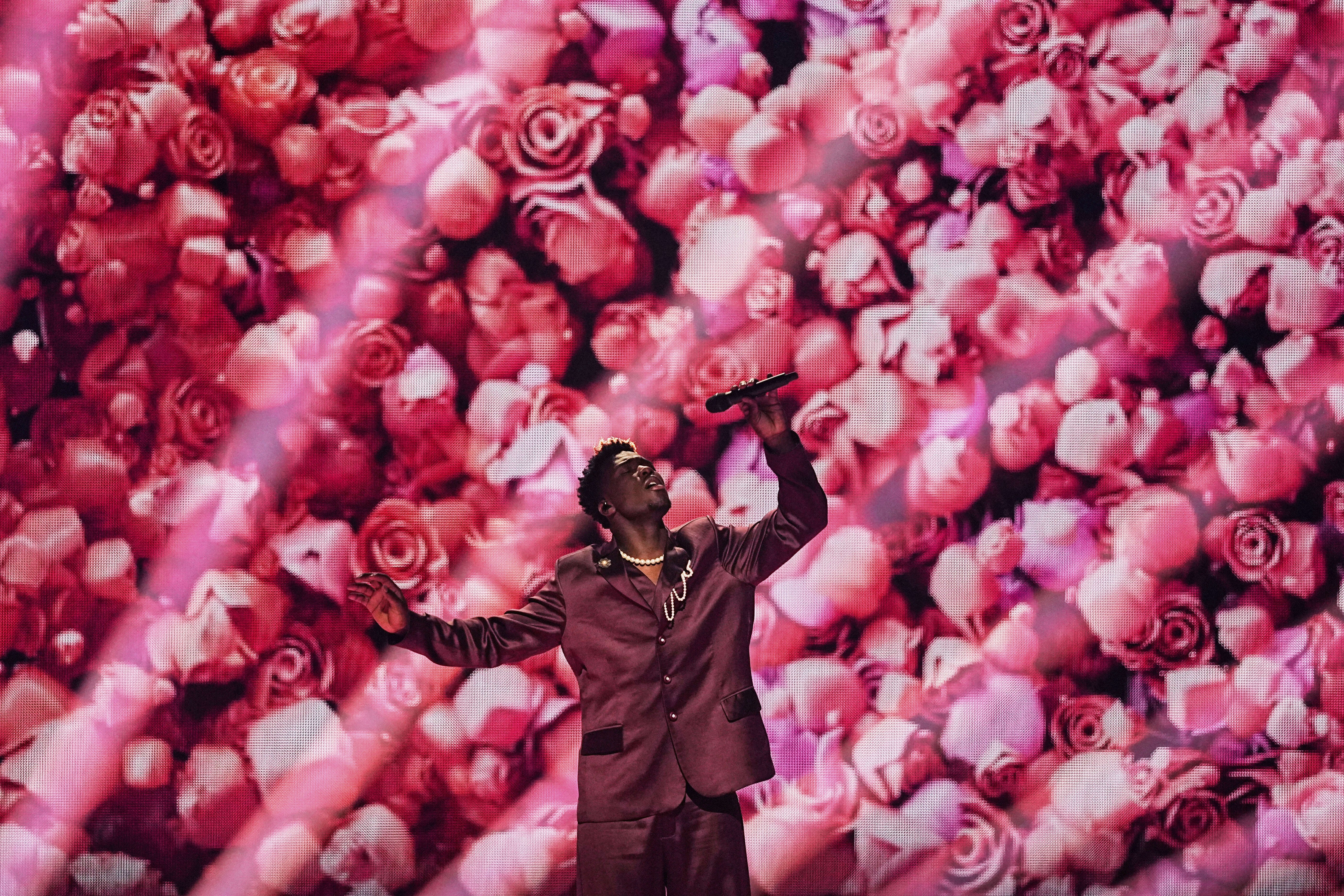 A singer performs in front of a large video screen, depicting many flowers.