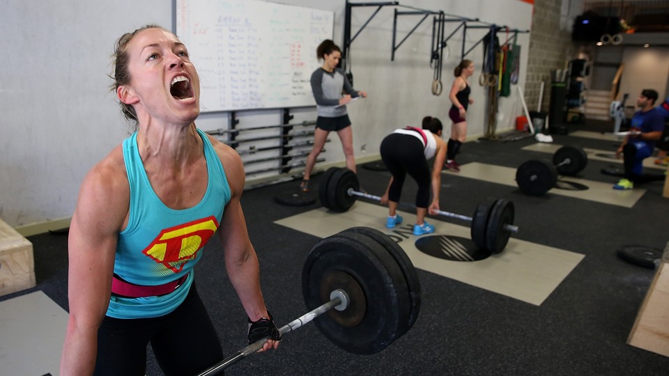 A woman makes an intense face while doing a deadlift during a CrossFit workout.