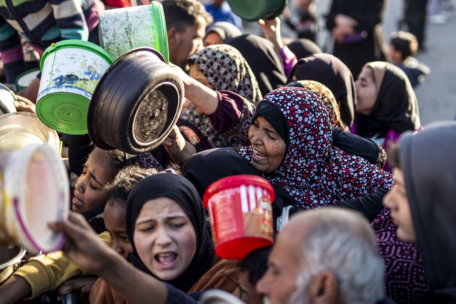 People in a crowd hold up plastic tubs while waiting for food handouts.
