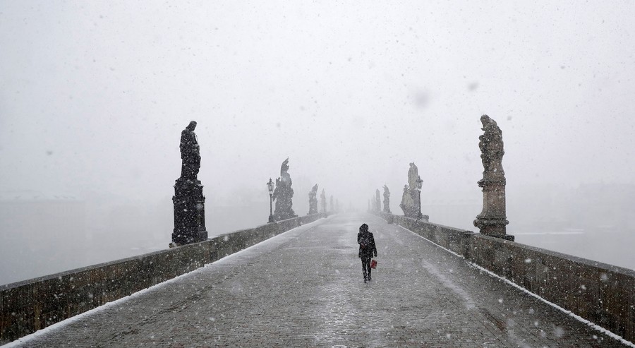 A woman walks across a bridge in a snowstorm.