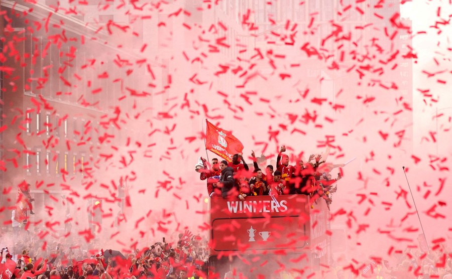 Confetti and red smoke fill the air as a soccer team celebrates aboard an open-top bus.