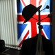 An image of a hat hanging on a hook in front of the Union Jack flag.