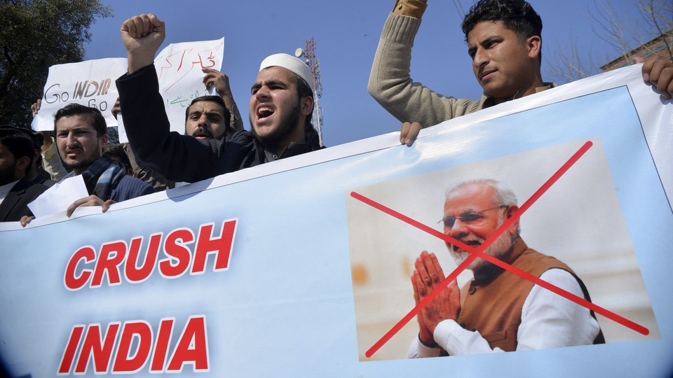 Pakistani men attend a rally with a banner that shows Indian Prime Minister Narendra Modi's face crossed out.