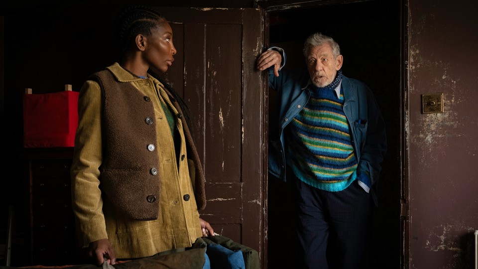 Michael Coel glances back at Ian McKellen, who stands in a doorway in an untended building.