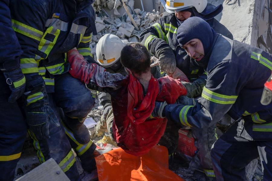 A person is lifted out of rubble by several firefighters.