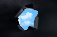 An illustration of a patch of blue sky appearing from behind torn black paper