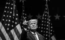 Black-and-white photograph of Donald Trump in front of some American flags
