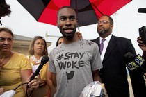 DeRay Mckesson speaks to the media, wearing a grey shirt that says 'Stay Woke.'