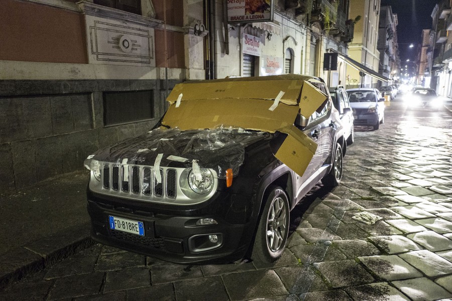 A car is parked on a street, covered in plastic and cardboard.