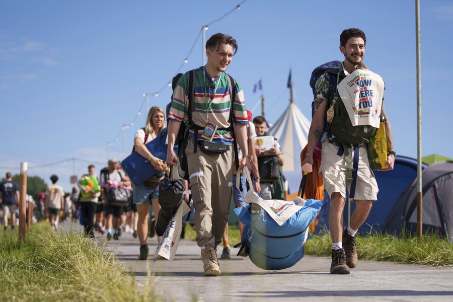 People walk on a path, carrying backpacks and camping gear.
