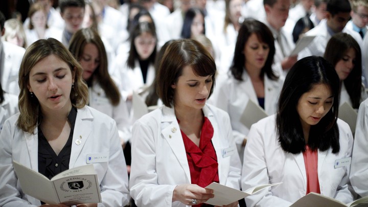 A group of students in white lab coats reads from pamphlets.