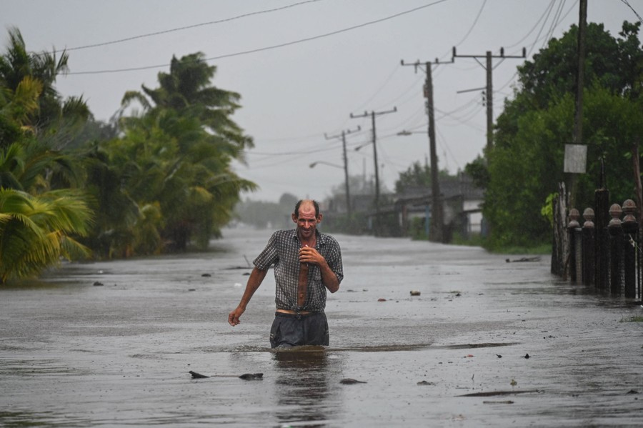A person weeds through hip-deep floodwater in a street.