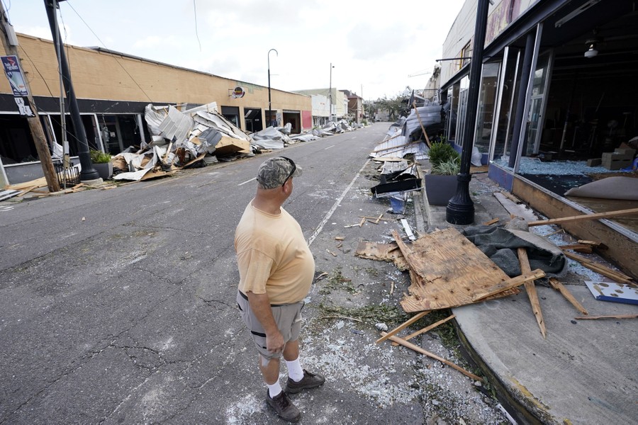 A man stands in a street looking at damaged storefronts.