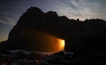 Sunlight passes through a natural arch on a seashore.