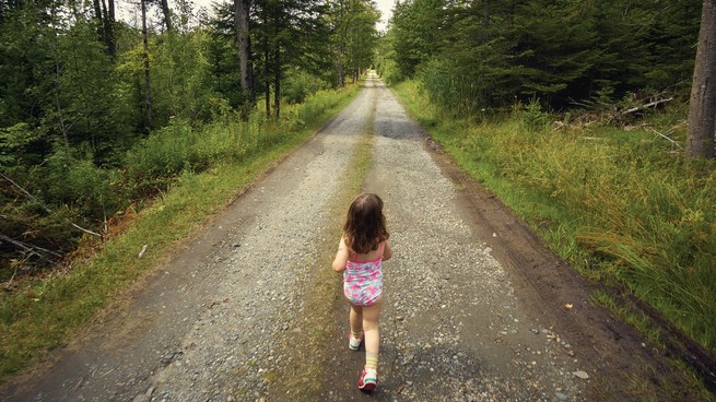 A little girl in a pink and bathing suit walks on a path in the woods